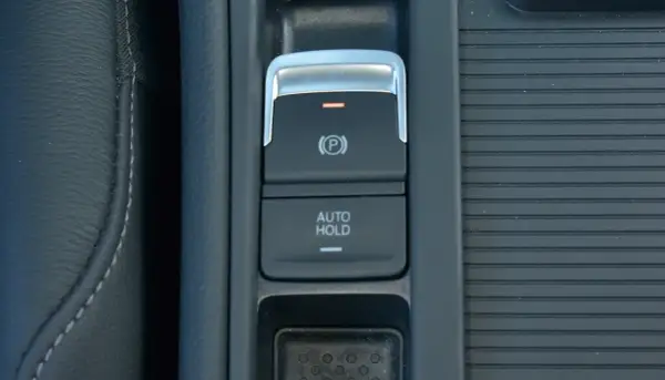 Przycisk "AUTO HOLD" w samochodzie, obok hamulca ręcznego. Ułatwia postój bez trzymania pedału hamulca.